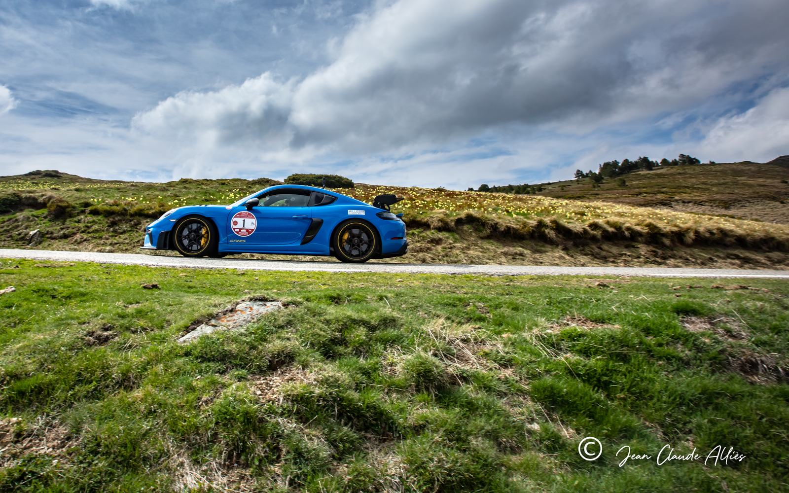 Porsche Cayman bleue sur une route de montagne, sous un ciel chargé