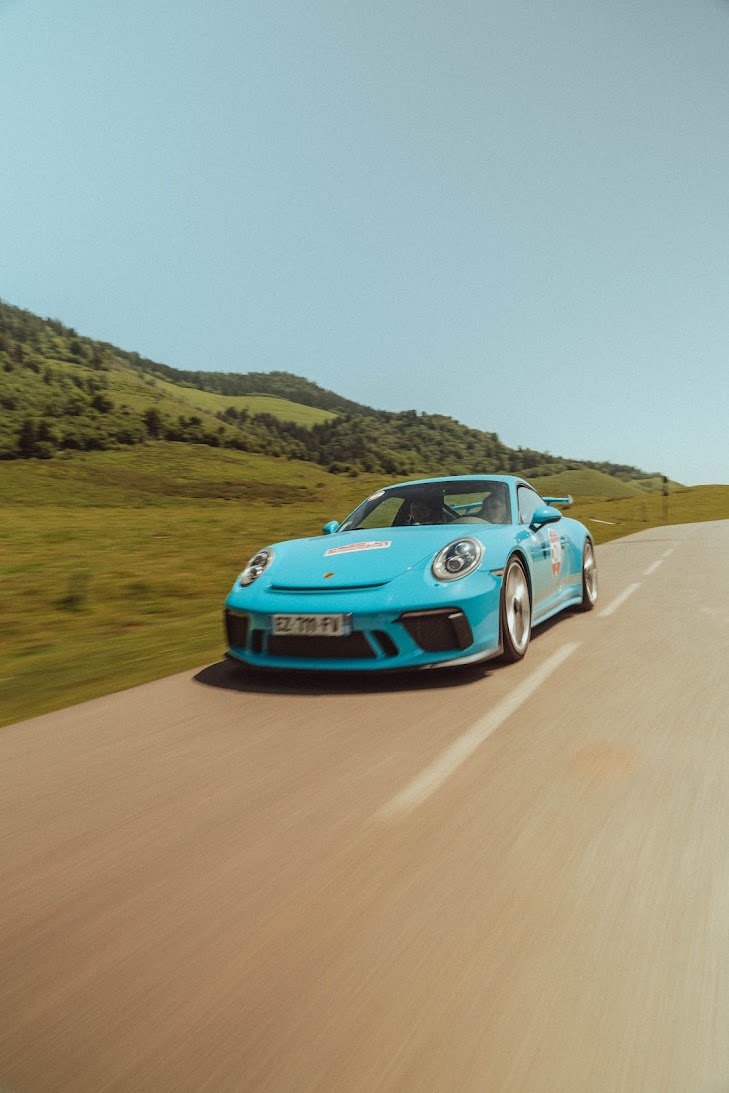 Porsche 911 bleu turquoise en mouvement sur une route de montagne